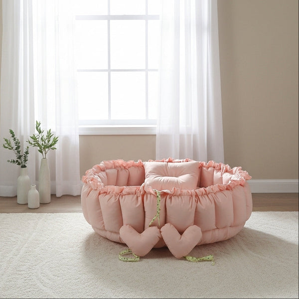 Pink pet bed with heart designs in a room with a window and plants.